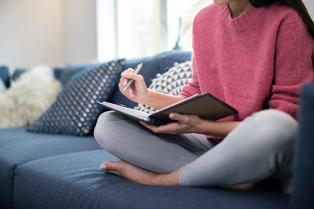 Close Up Of Young Woman Relaxing On Sofa At Home Writing In Jour